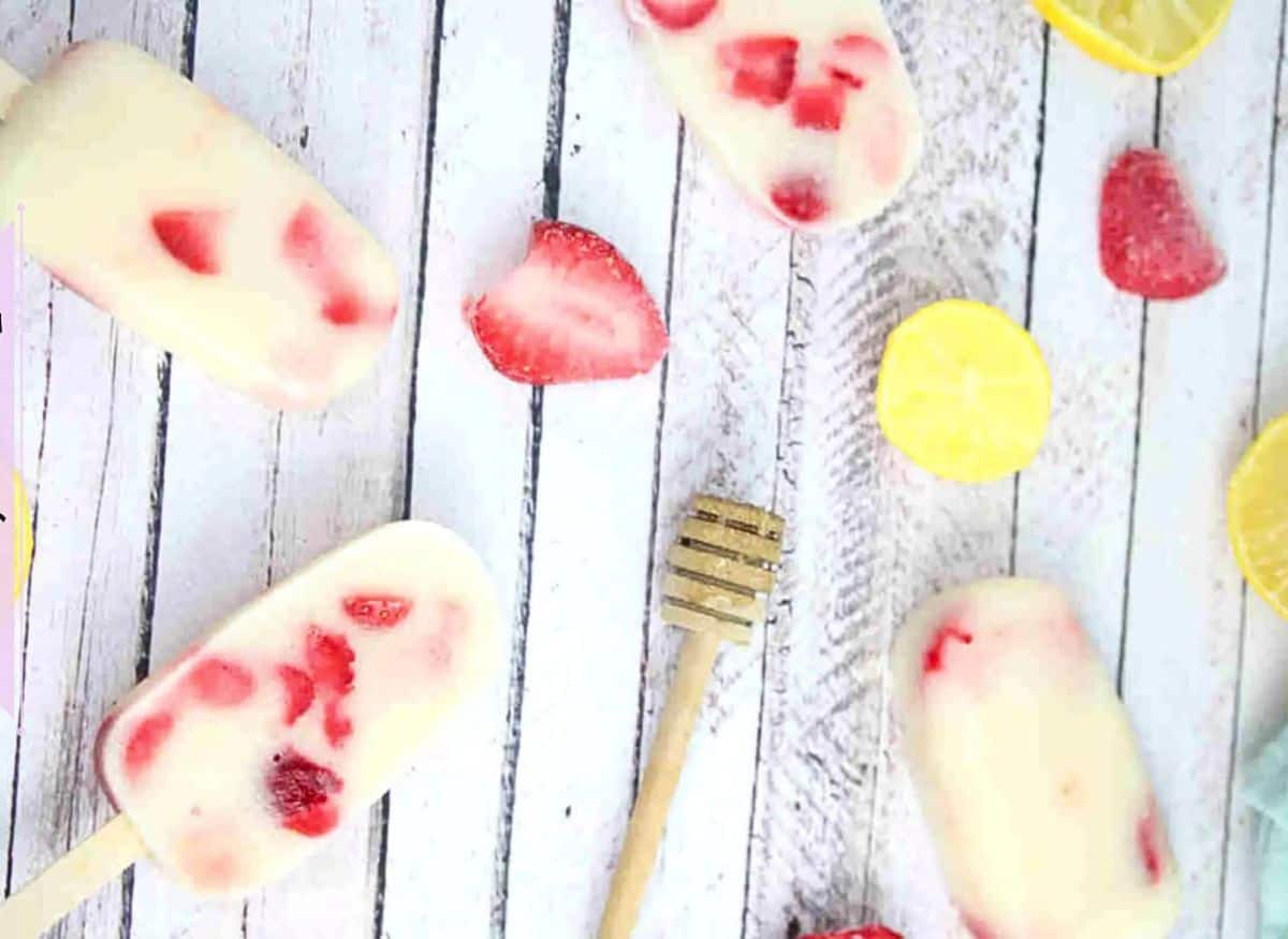Protein popsicles with strawberries in a white silicone mold with berries, lemon, and honey around them.