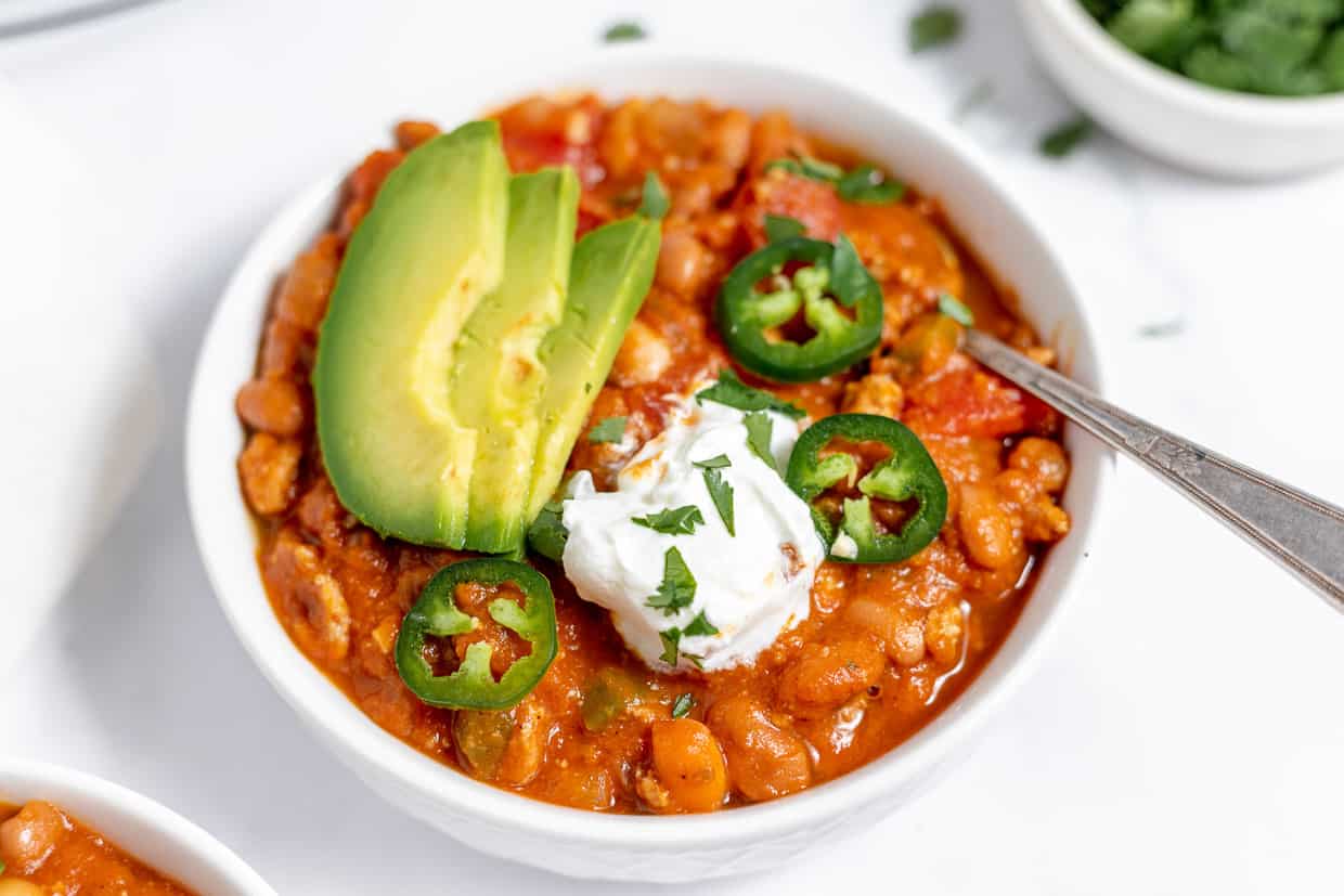 A bowl of chili topped with avocado and peppers.