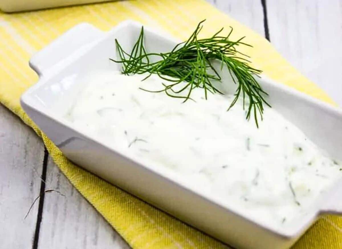 A bowl of dill dip with a sprig of dill.