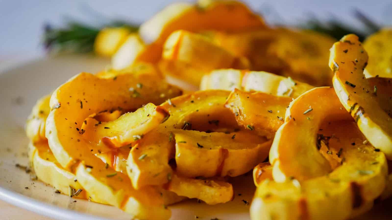 Roasted squash slices on a plate with rosemary sprigs.