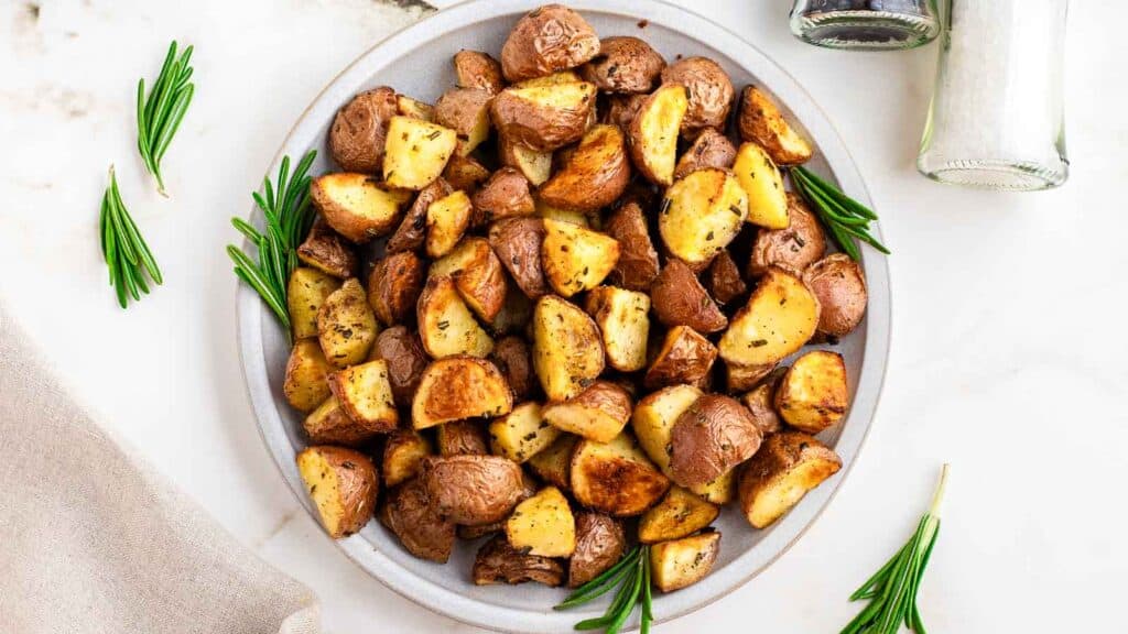Air fryer red potatoes on a white plate with fresh rosemary sprigs.