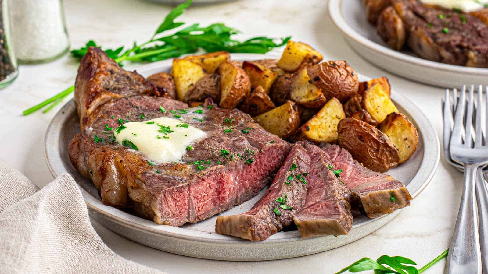 Air fryer ribeye on a plate with potatoes and butter.