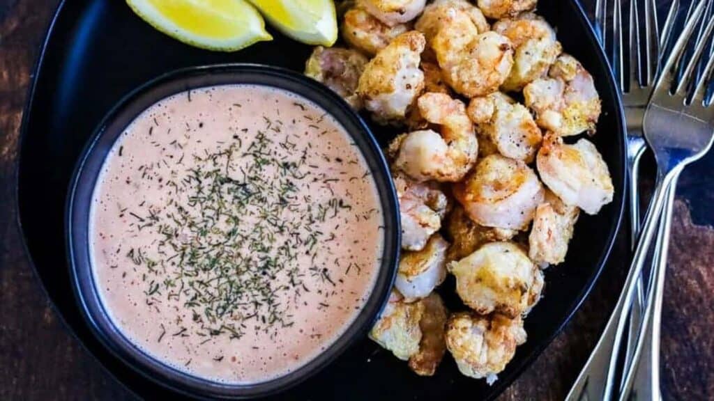 Shrimp skewers with dipping sauce on a black plate.