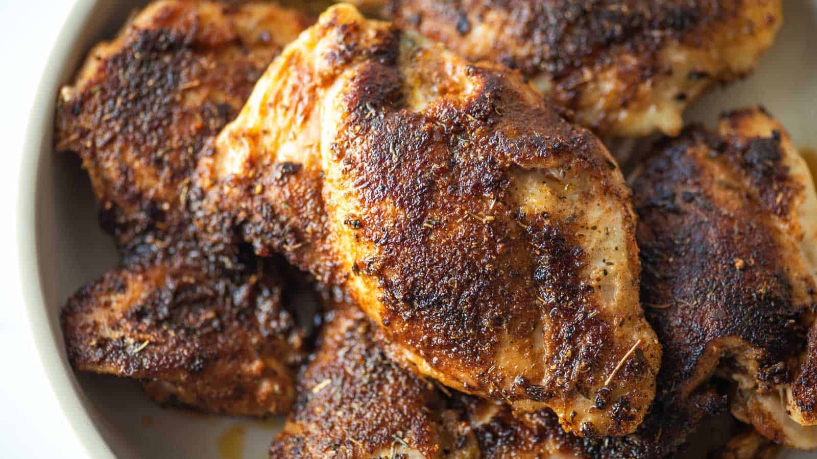 Blackened chicken thighs in a white dish.
