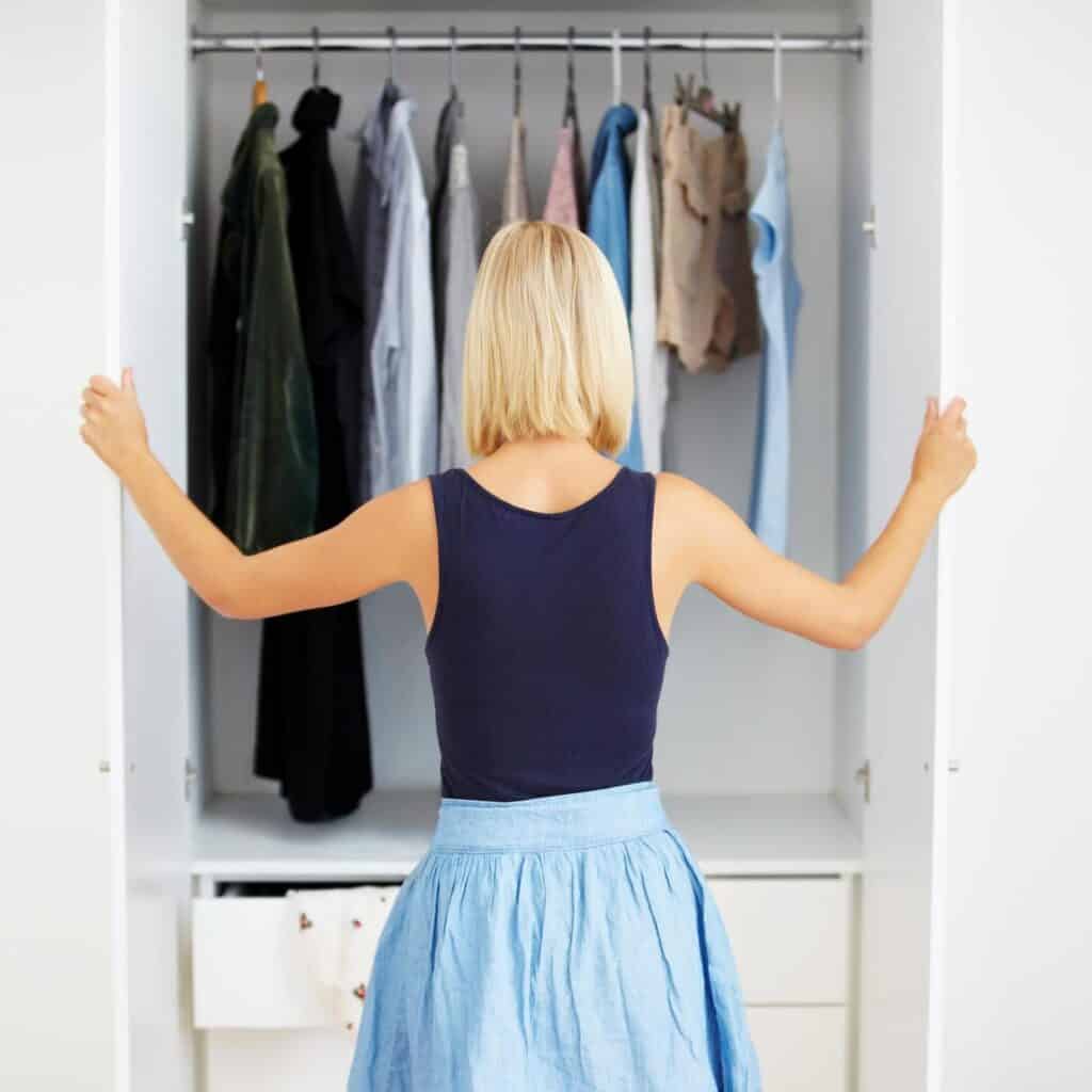 A woman curating a capsule wardrobe in front of a closet full of clothes.