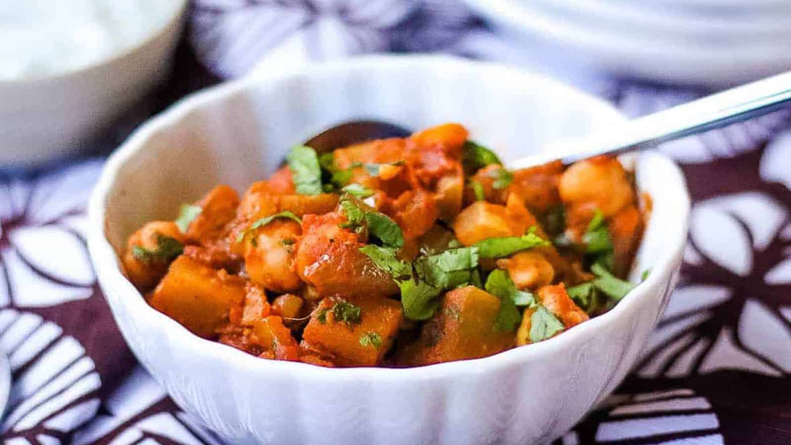 Chana aloo masala in a white bowl with a spoon, on top of a brown and white linen.
