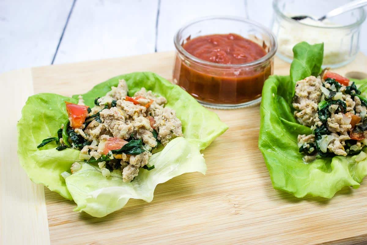 Two lettuce wraps with chicken and spinach on a cutting board.