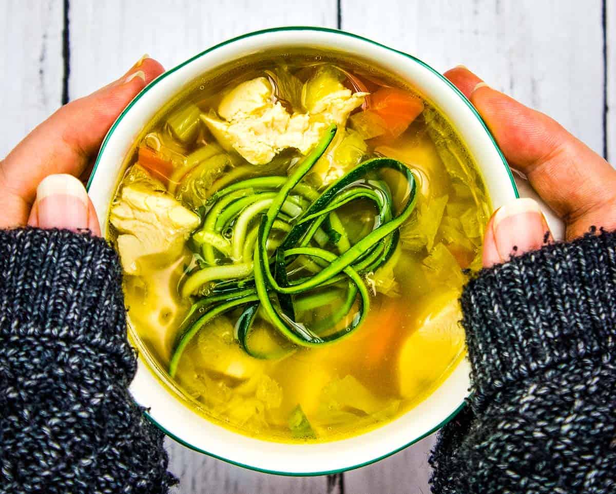 Hands holding a bowl of Chicken Zoodle Soup.