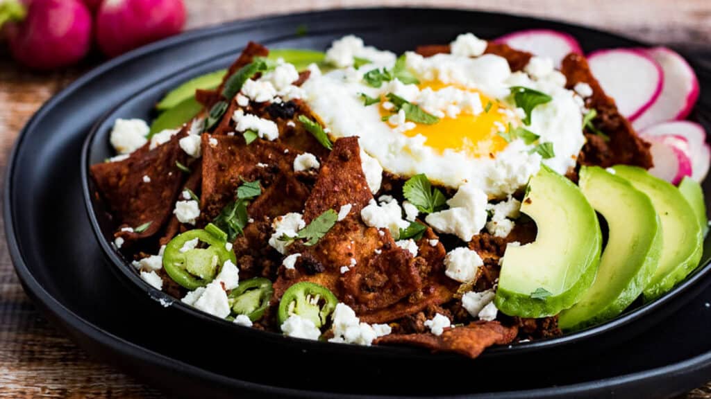 A bowl of nachos with avocado, radishes and an egg.