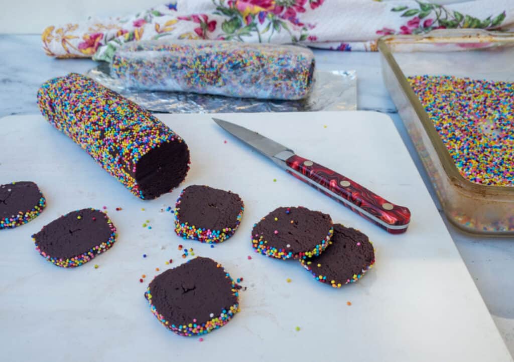 A chocolate roll with sprinkles and a knife on a cutting board.