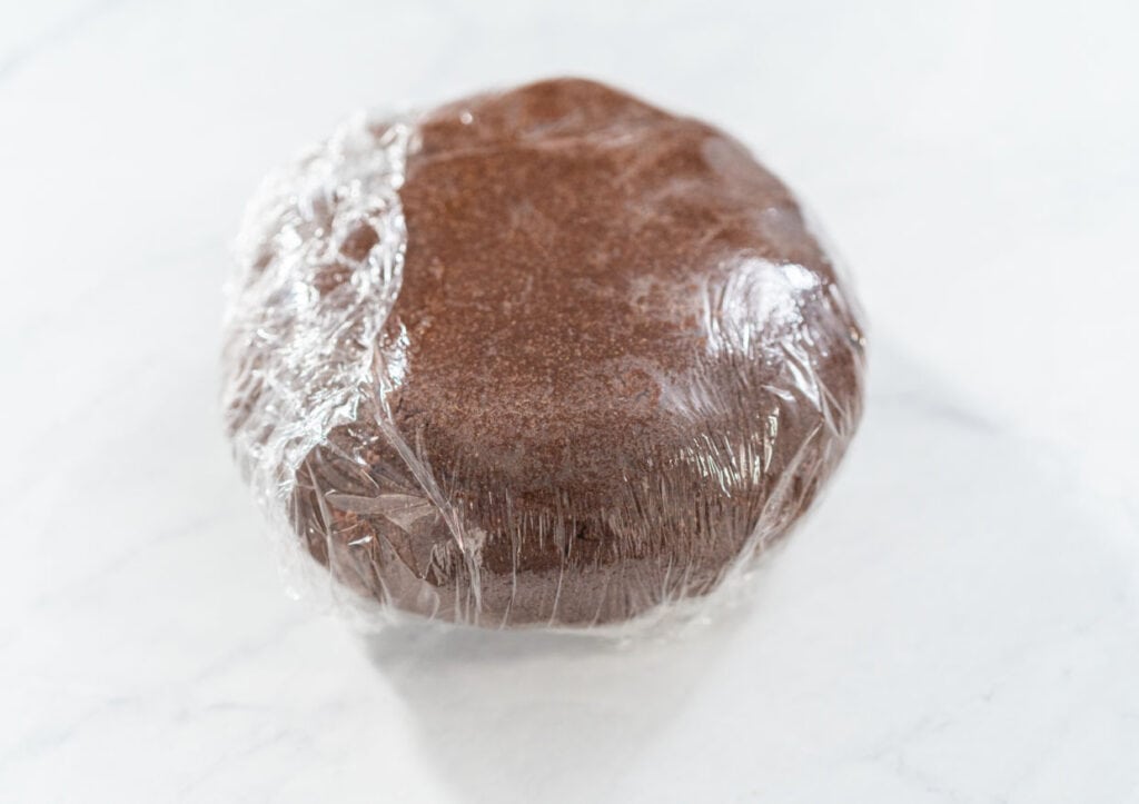 A chocolate cookie dough ball wrapped in plastic on a marble surface.