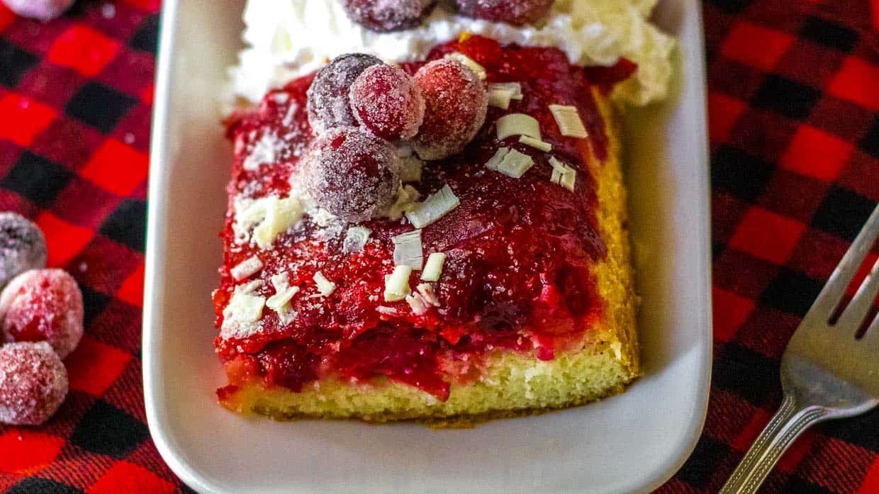 A slice of cranberry cake on a plate with whipped cream.