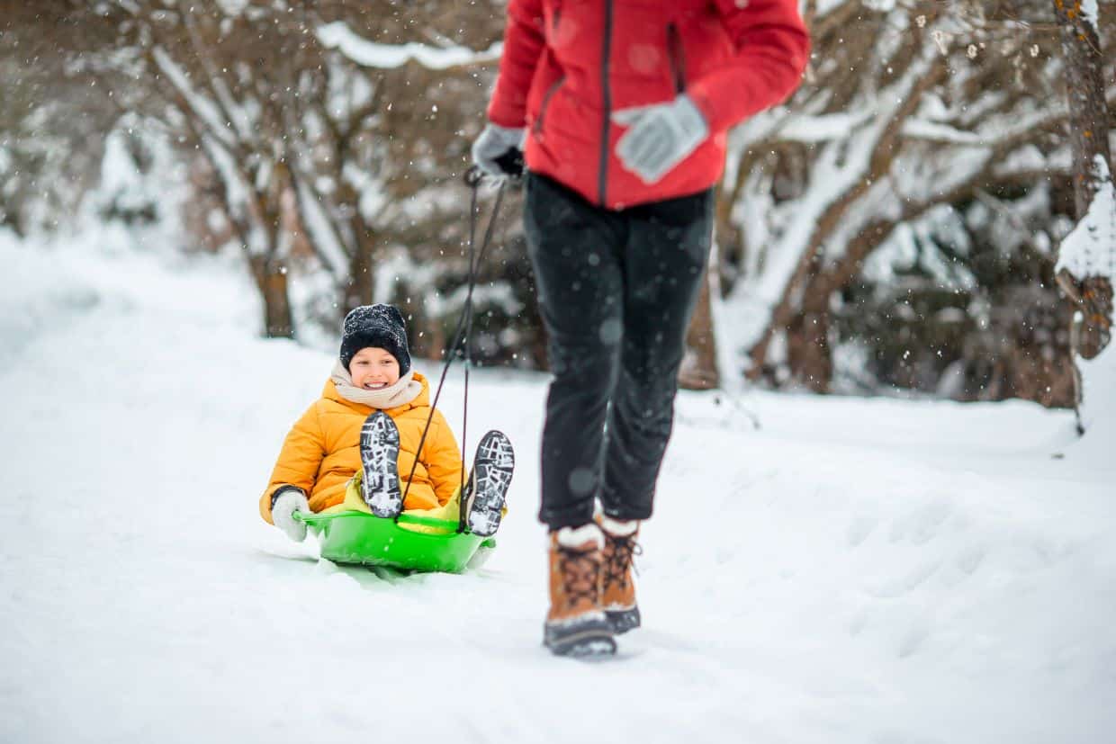 A man is pulling a child on a sled down a snowy path.