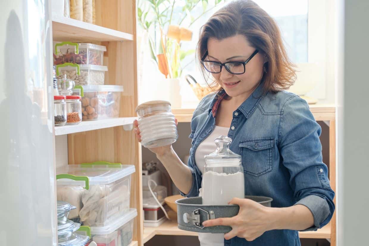 A woman is picking dry goods from the pantry shelf.