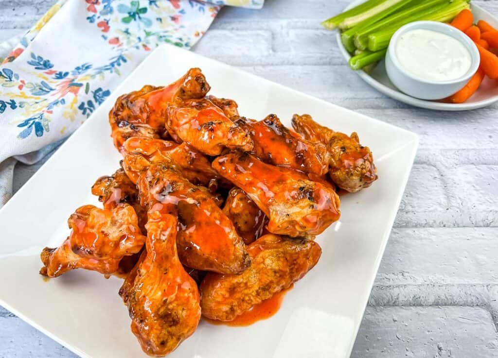 Buffalo wings on a white plate with carrots and celery.