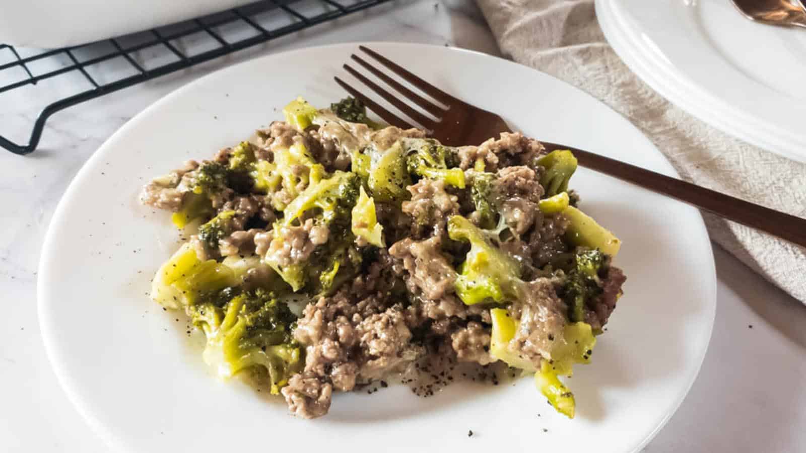 A plate of ground beef and broccoli casserole on white plate with a copper fork.