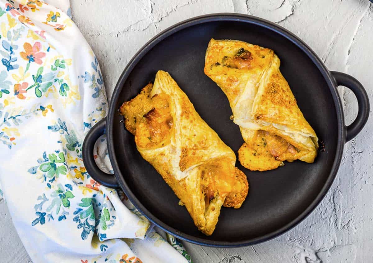 Two ham and cheese turnovers in a pan on a table.