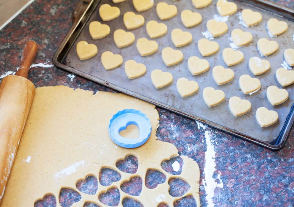 Heart shaped cookies on a baking sheet with a rolling pin.