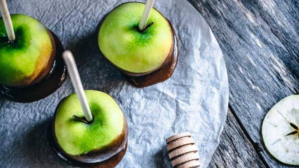 Three caramel covered apples on a plate.