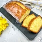 A slice of lemon pound loaf on a plate with daffodils.