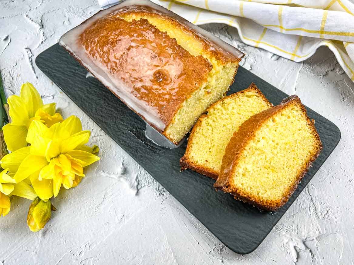 A slice of lemon pound loaf on a plate with daffodils.