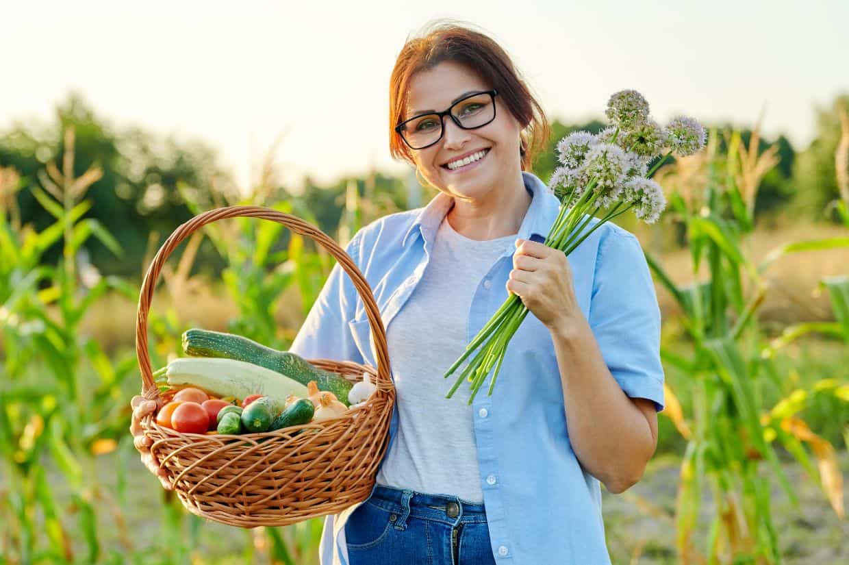 A woman holding a basket of local vegetables in a corn field.