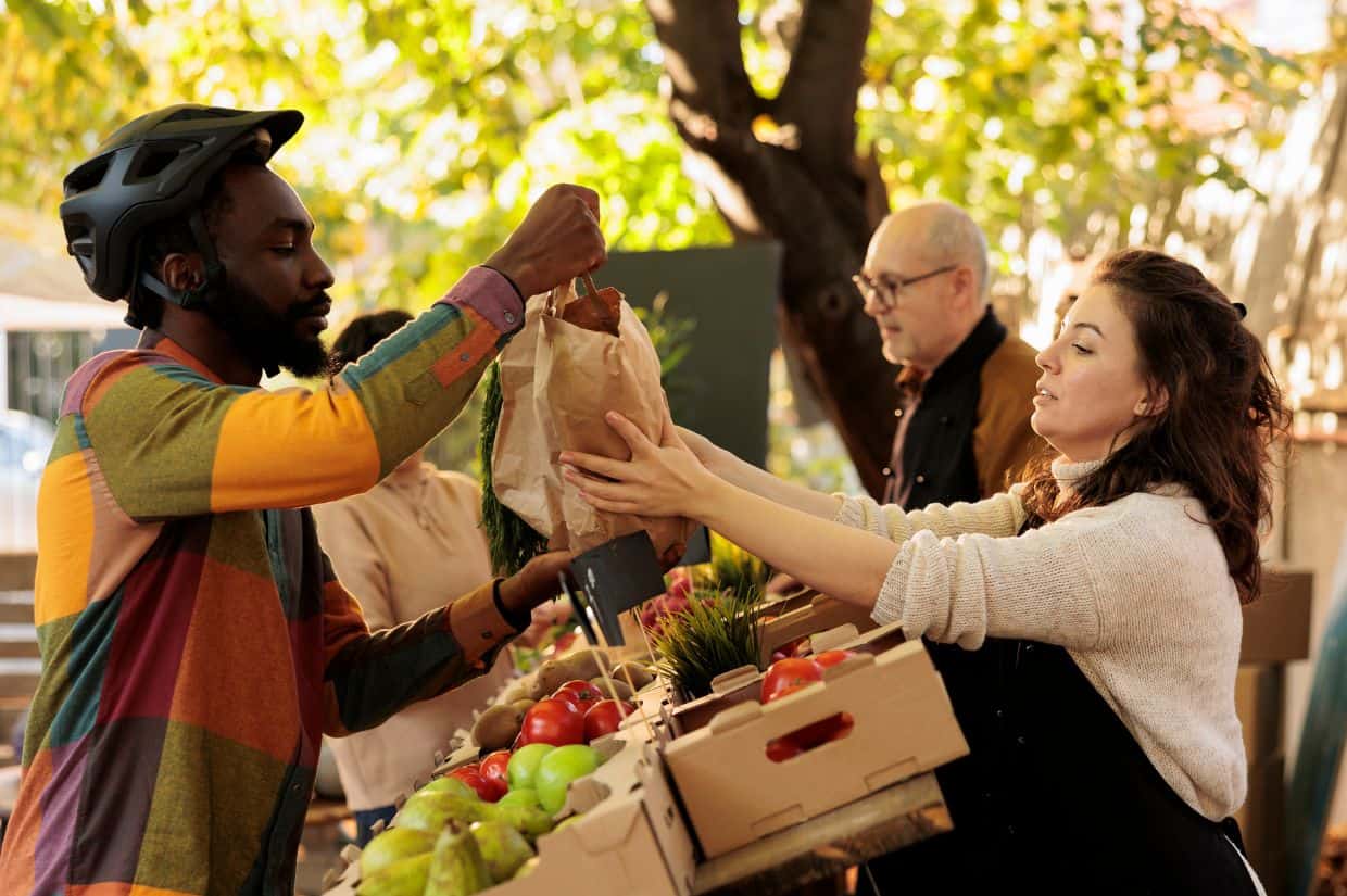 A man is handing a woman a box of locally sourced vegetables.