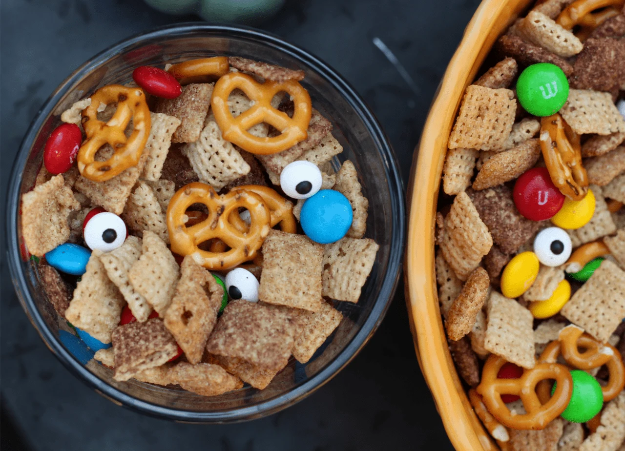 Glass bowl of monster chex mix next to a yellow bowl.