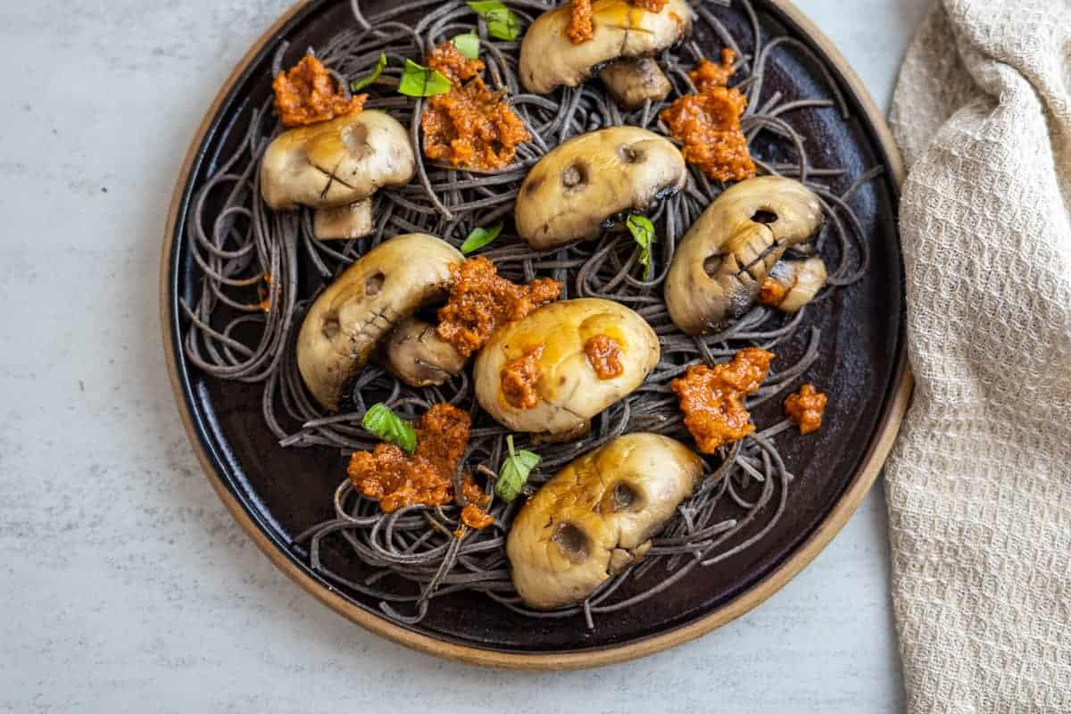 Mushrooms in the shape of skulls on a plate of black spaghetti.