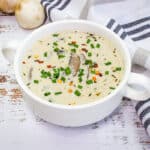 A white bowl of soup with mushrooms and chives.