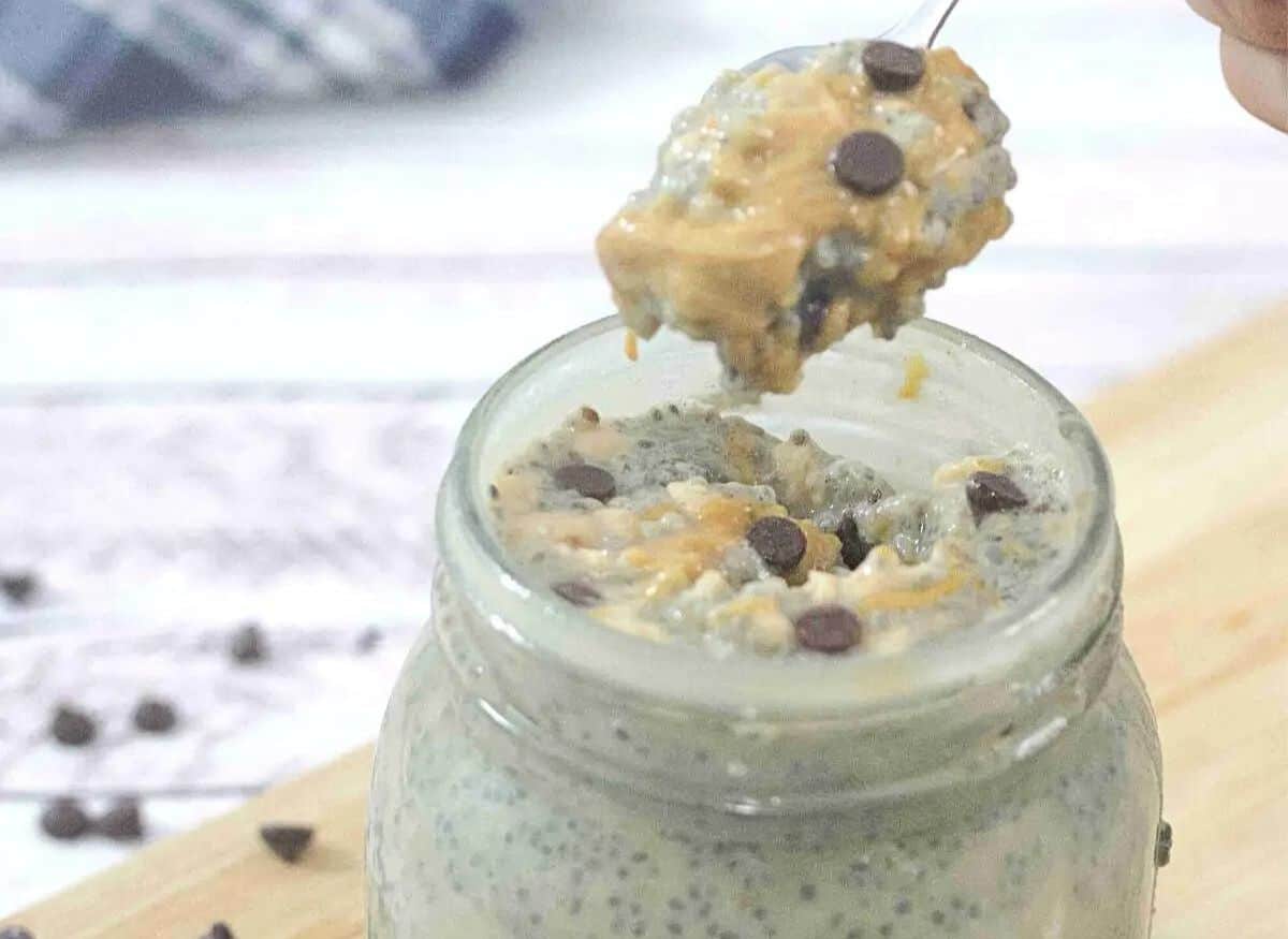 Peanut butter chia pudding with chocolate chips in a mason jar on a cutting board with more chocolate chips around it.