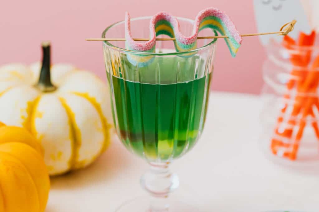 A green drink in a glass next to a pumpkin.