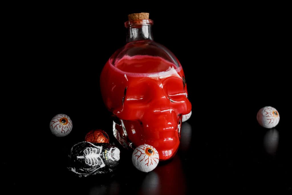 A bottle of red liquid with a skull on it.