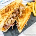 A pulled pork sandwich with fries on a slate board.