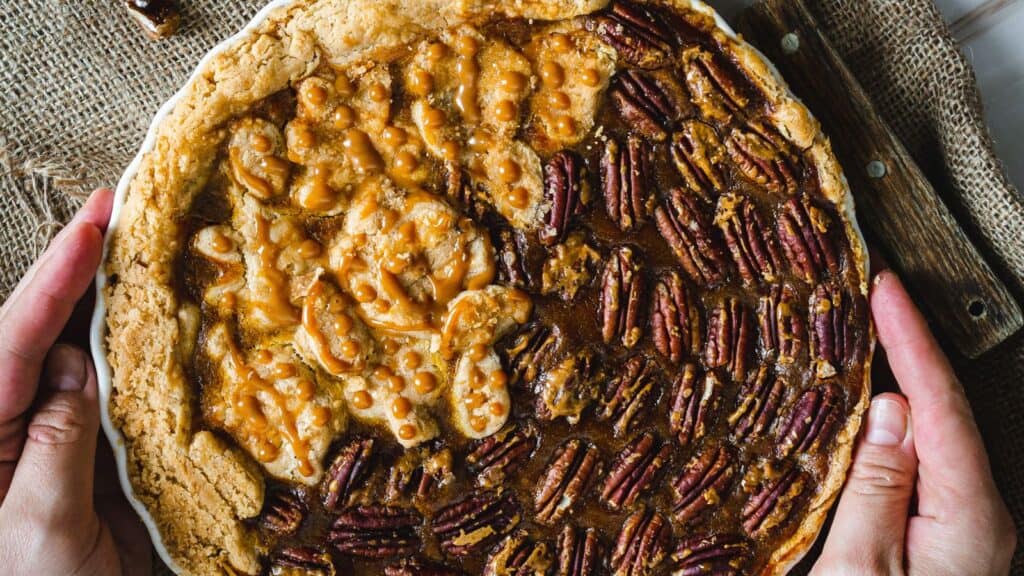 A person holding a pie with pecans on it.