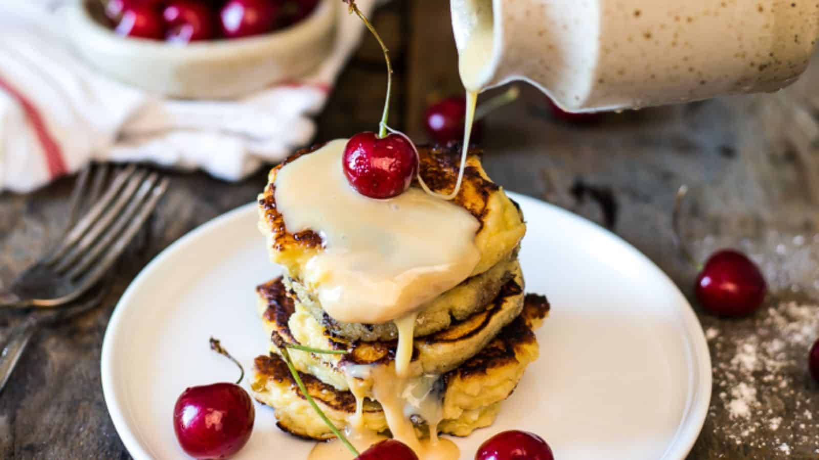 A stack of classic pancakes with a cherry sauce being poured on top.