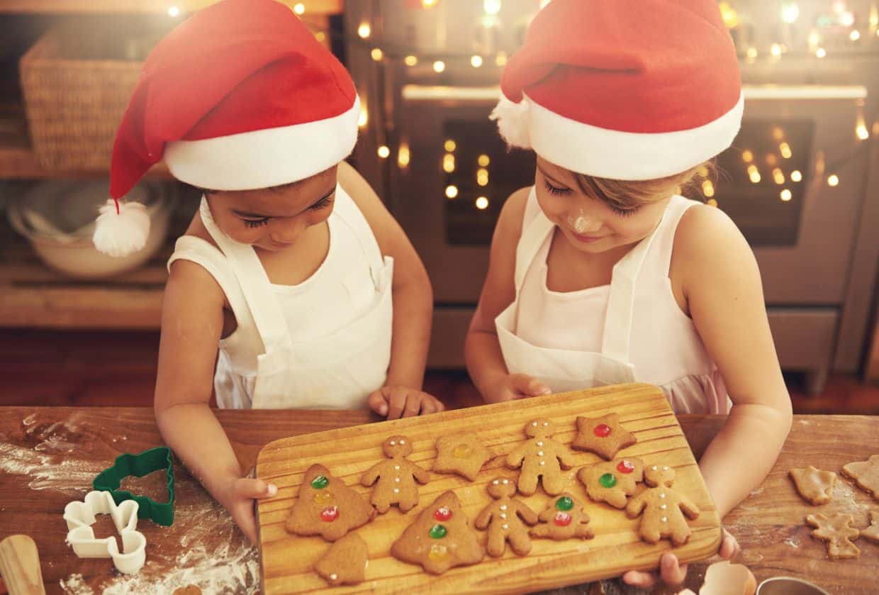 Two children in santa hats making gingerbread cookies.