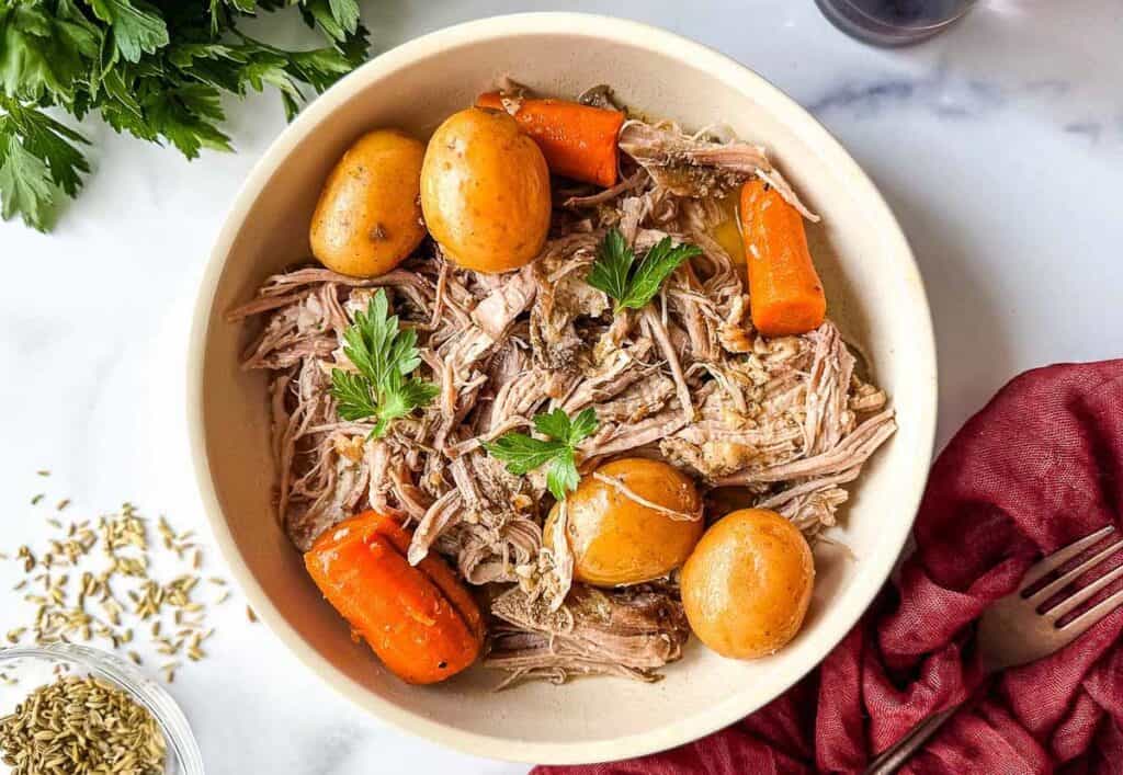 A bowl of roast pork with carrots and potatoes.