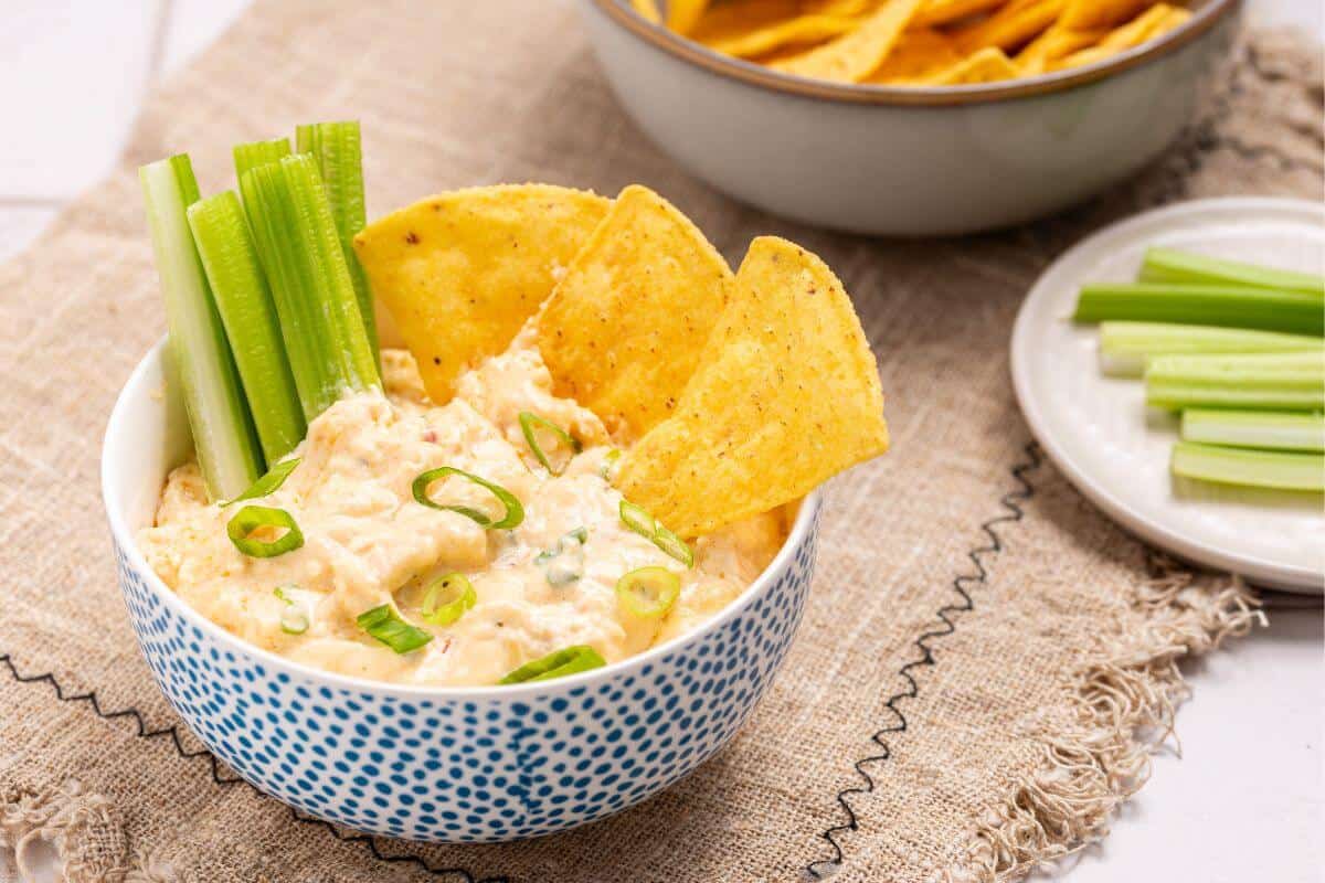 A bowl of buffalo chicken dip with celery and chips.