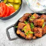 A plate of smoked pork belly burnt ends with tomatoes and pickles.