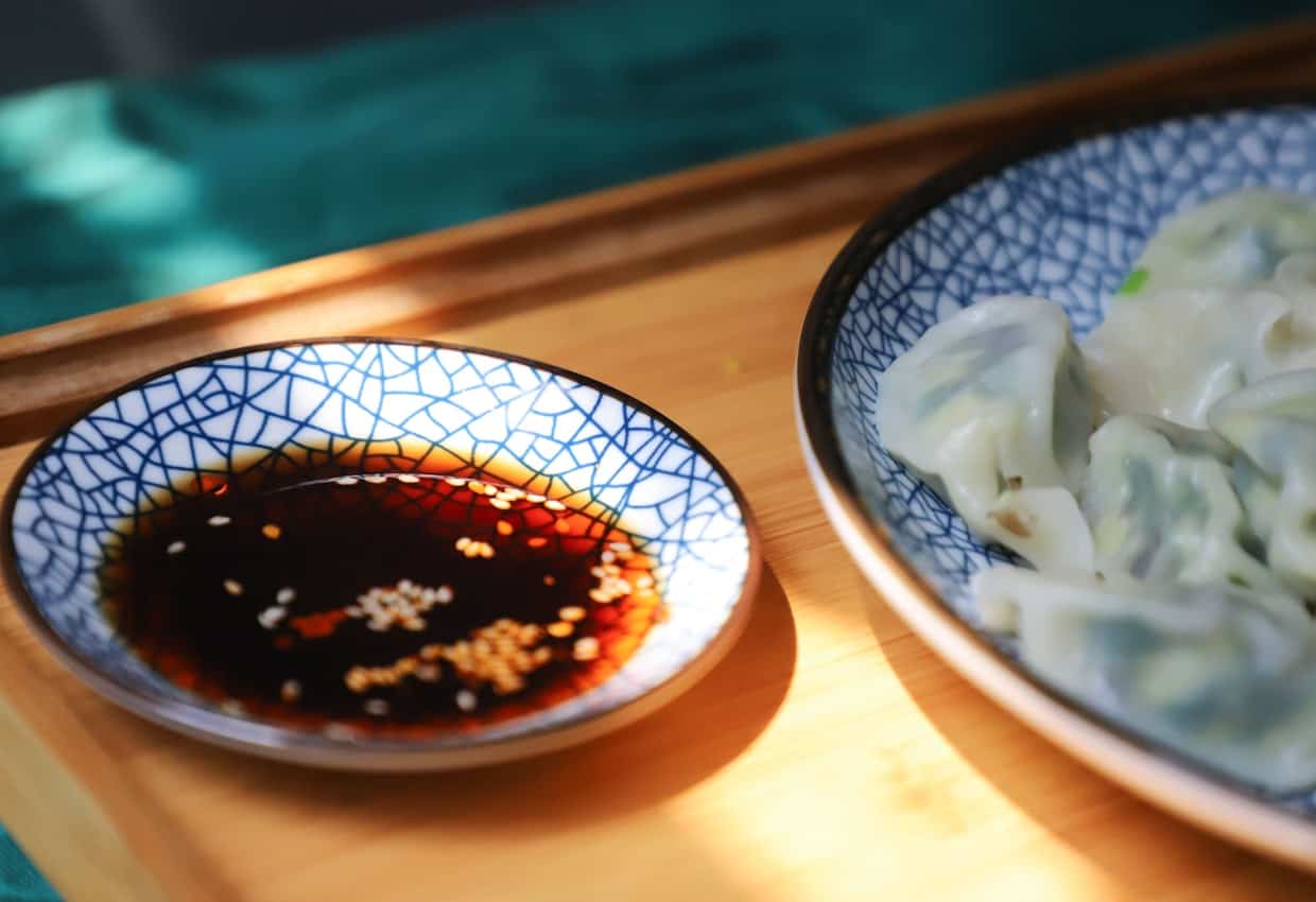 A bowl of dumplings with soy sauce on on the side on a wooden tray.