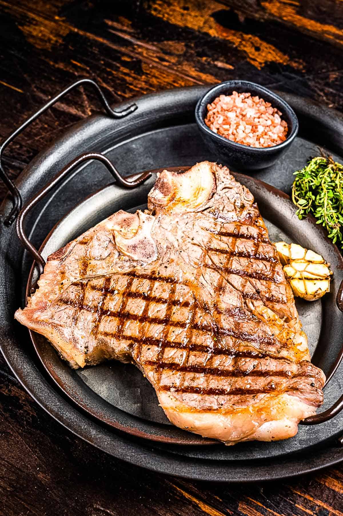 A grilled t-bone steak on a black platter.