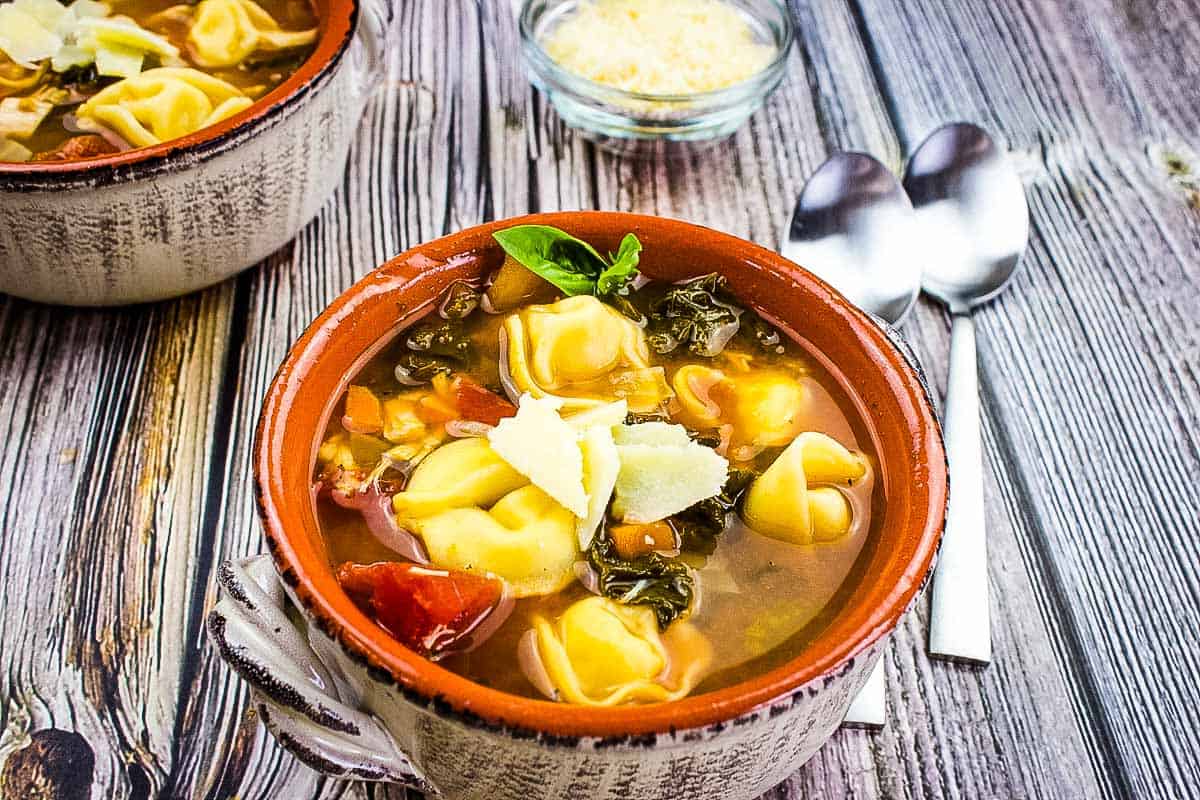 Kale and tortellini soup in a bowl on a wooden table.