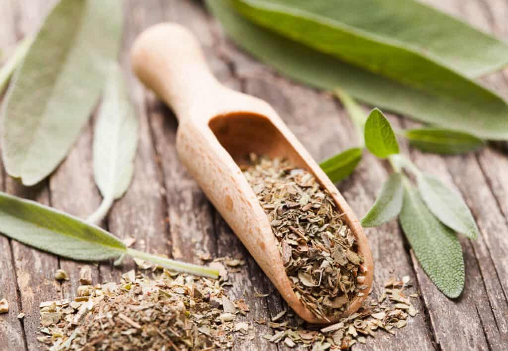 Sage leaves and a wooden spoon on a wooden table.