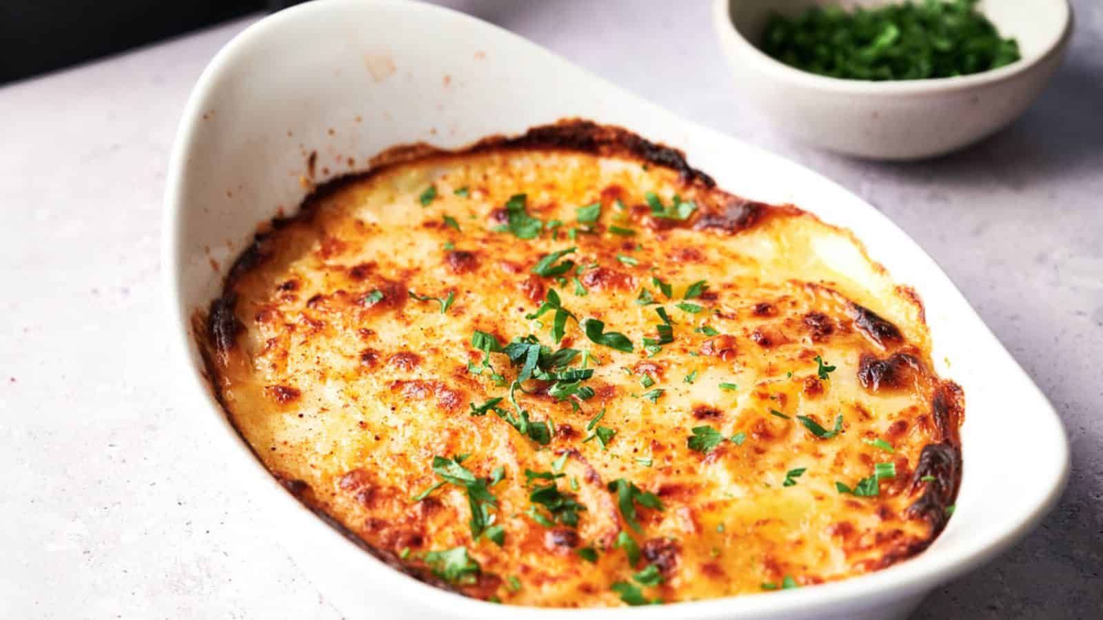 A white dish with scalloped potatoes and parsley.