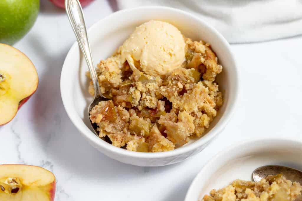 A bowl of apple crumble with ice cream and apples.