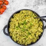 Arroz Verde rice in a black pan with tomatoes and herbs.