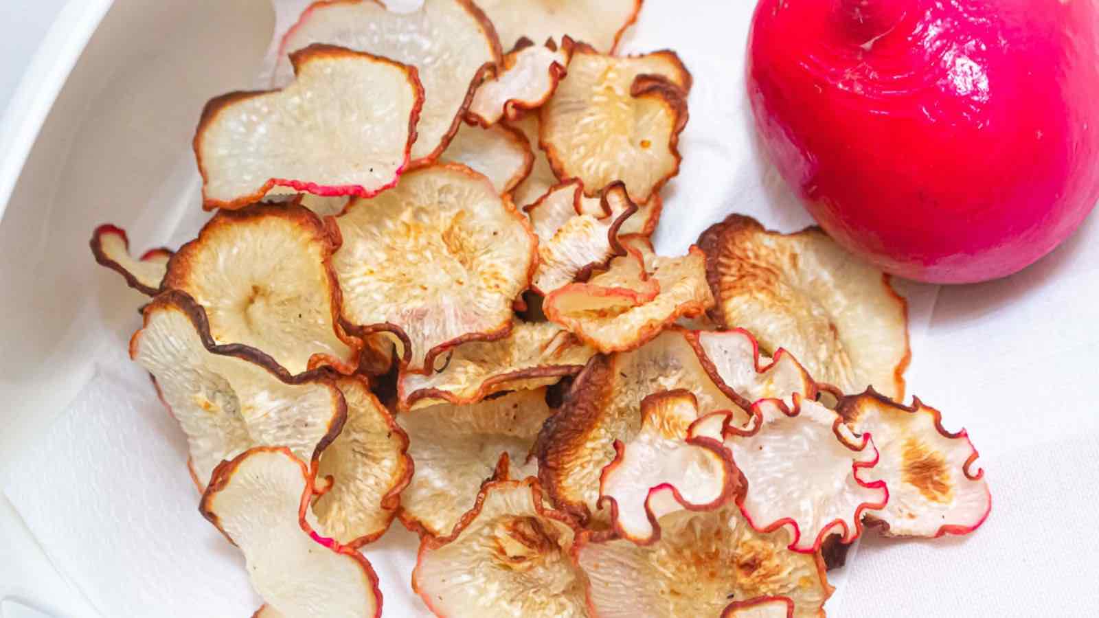 Sliced radishes on a white plate next to a red radish.