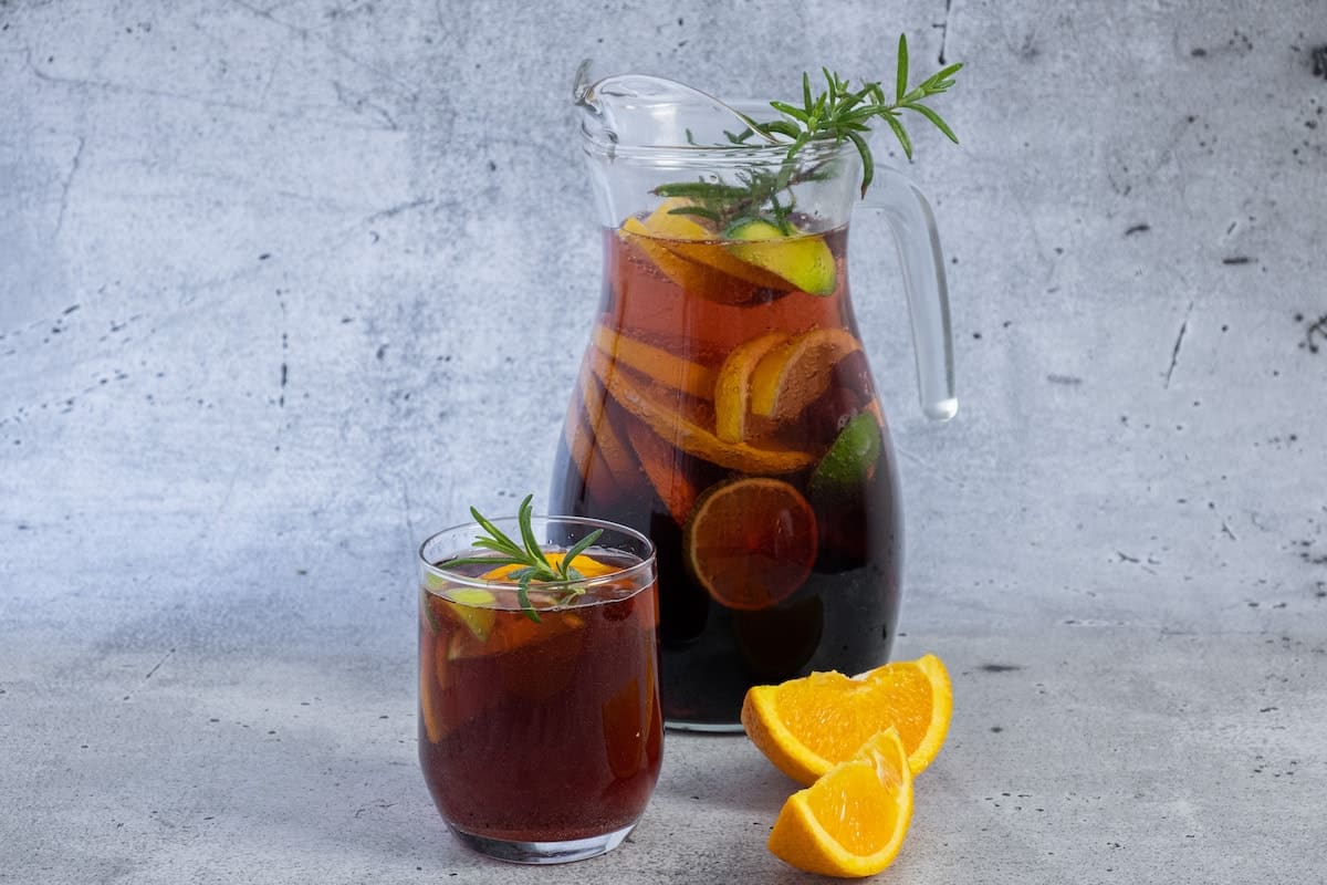 A pitcher of sangria with orange slices and sprigs of rosemary garnish.	