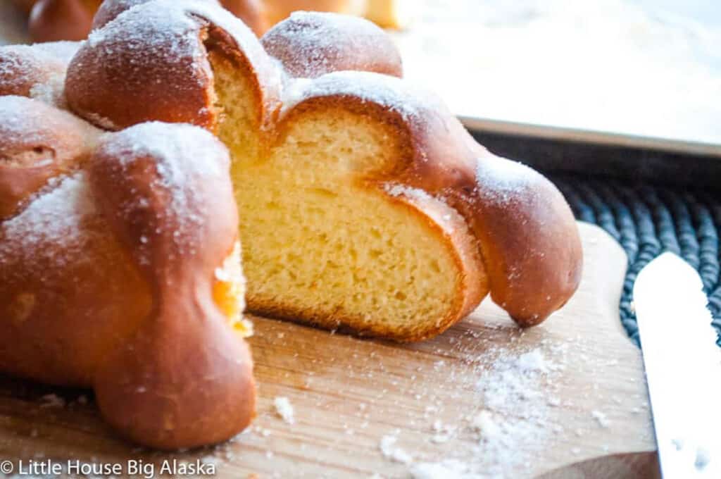 A Pan de Muerto with powdered sugar on a cutting board.